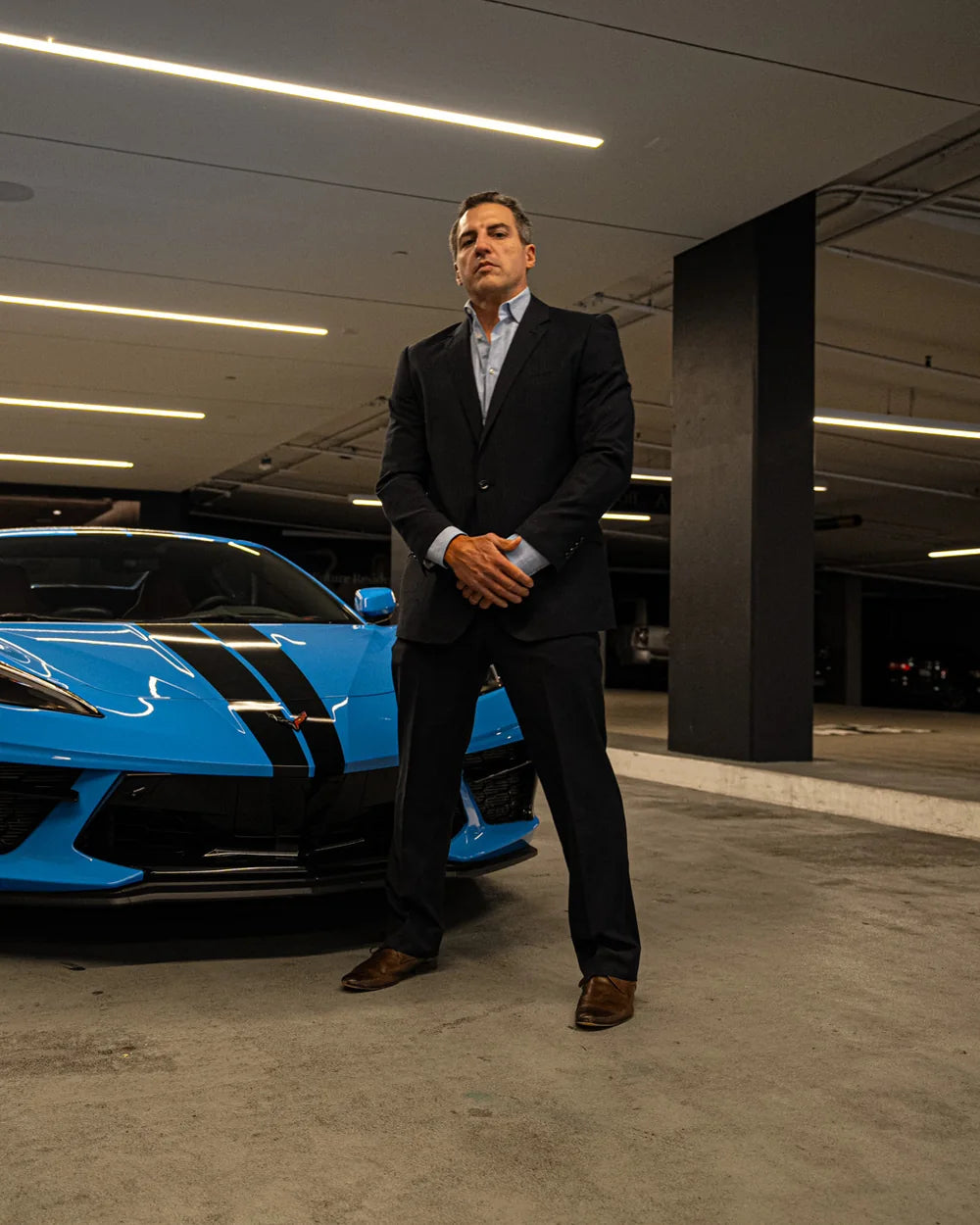 Matt Balzano in a dark suit beside a blue sports car