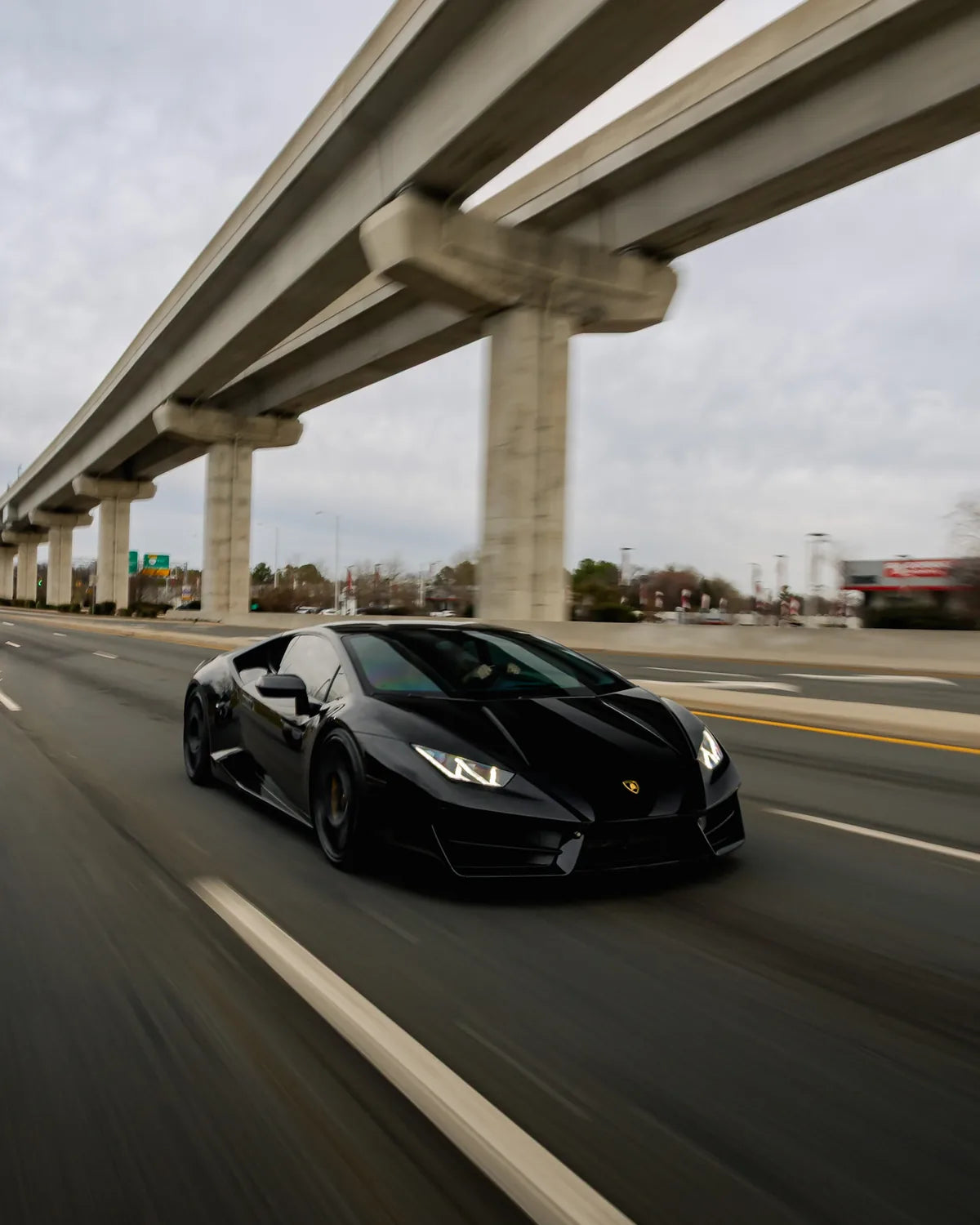 Black sports car photographed in motion beneath an overpass
